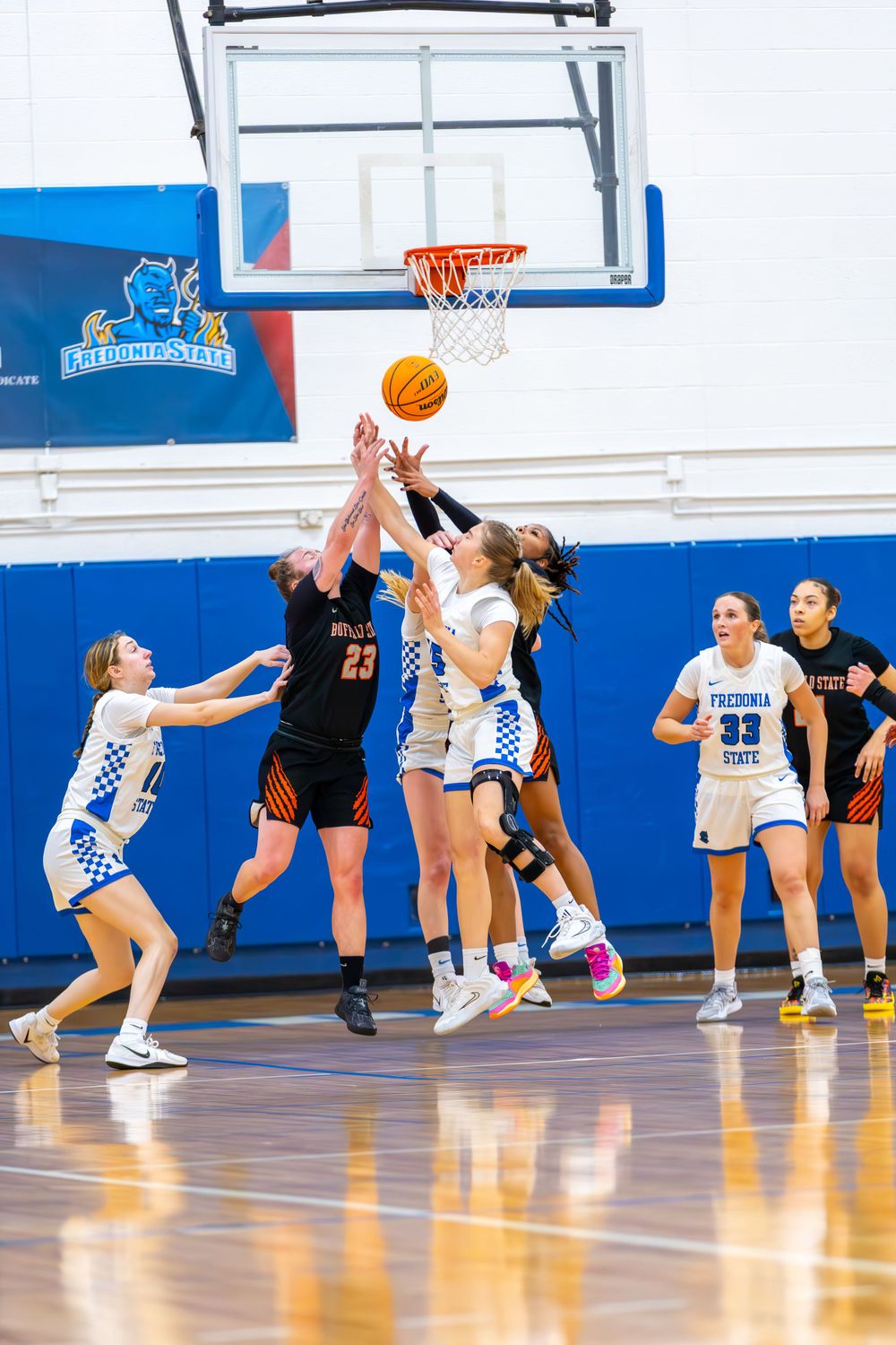 Basketball players jump for the ball during a game on a polished hardwood court.