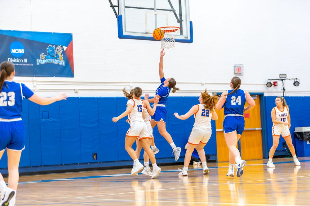 Basketball players position themselves for a shot during a game in a blue and white gymnasium.