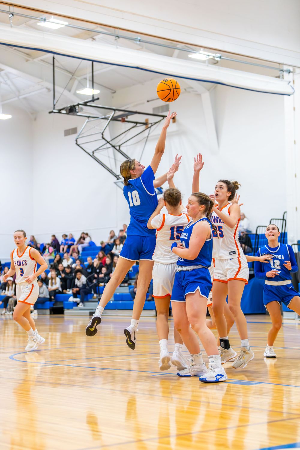 Players jump for a rebound during an intense women's basketball game on a bright indoor court.