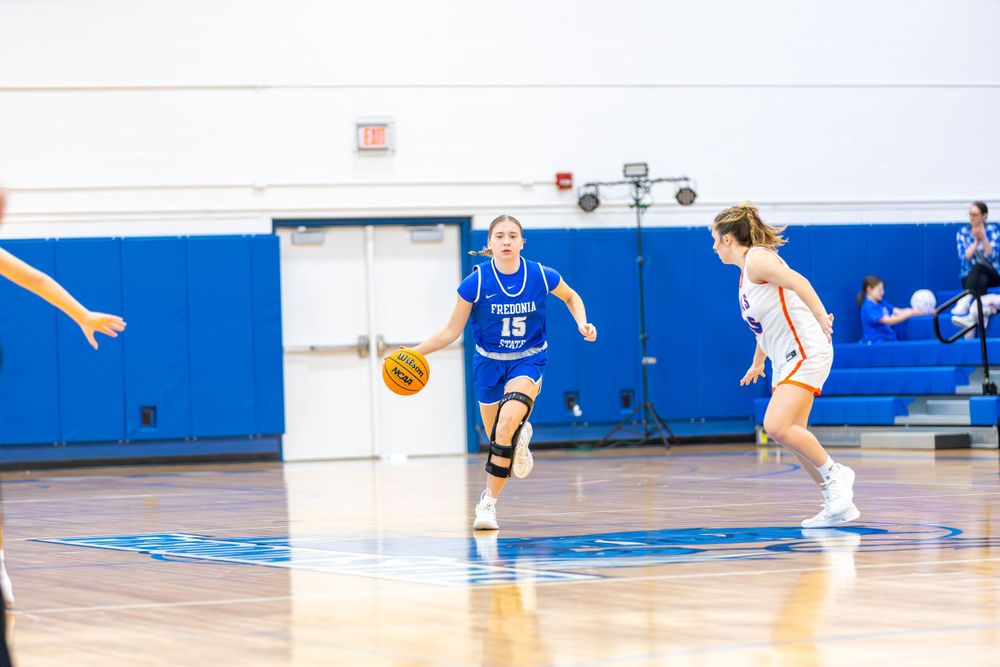 Basketball players spread across the court during an offensive play in a school gymnasium.