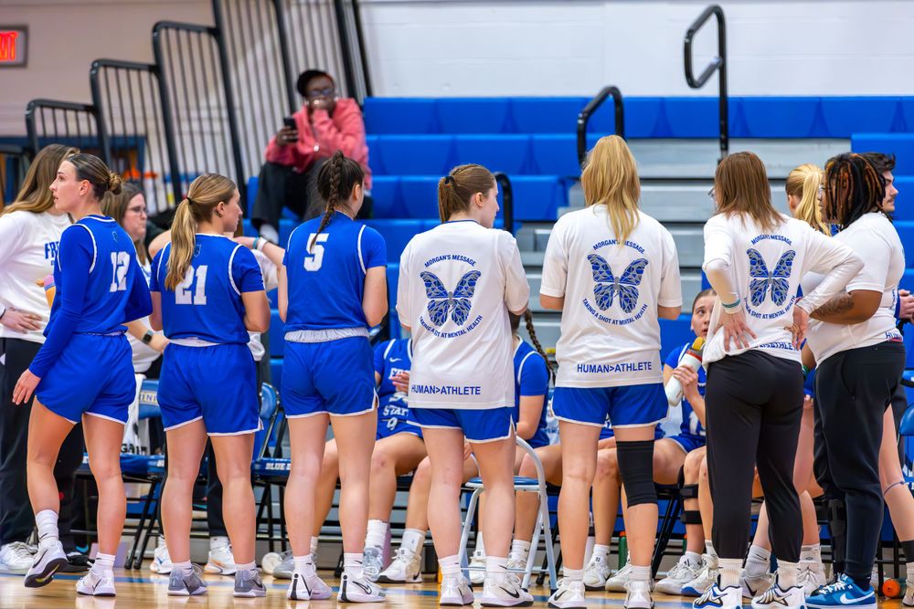 Players and coaches sit on benches along the sideline during a basketball game.