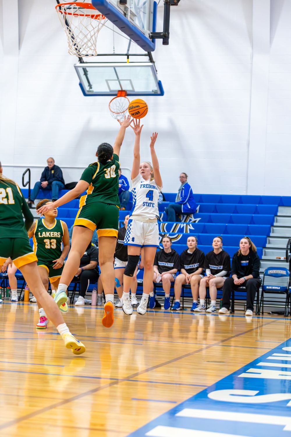 Women's basketball teams in green and white uniforms battle under the hoop during a competitive game.