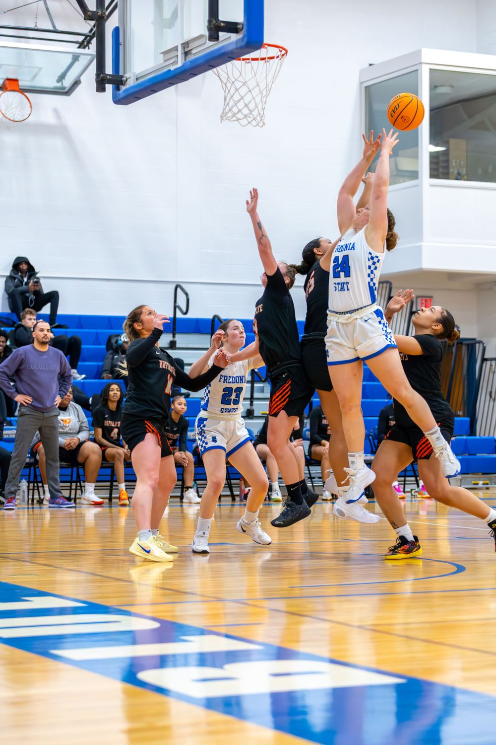 Athletes compete for rebounds and loose balls during an indoor basketball game.