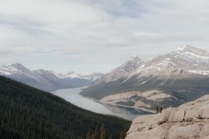 Scenic mountain landscape with snow-capped peaks and winding lake surrounded by dense evergreen forest. Archival photography print for home.