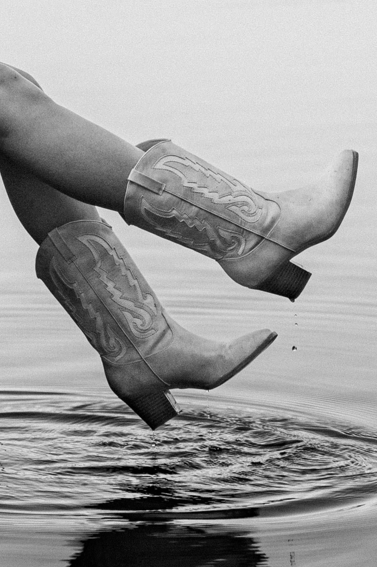 Artistic black and white photo of cowboy boots reflecting in still water.