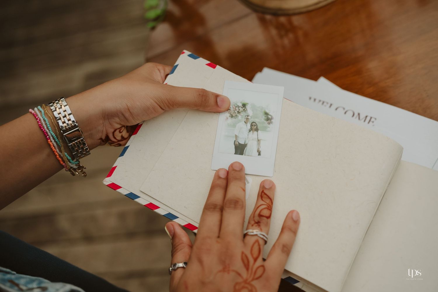 Close-up of hands writing in a guest book with decorative envelopes on wooden surface.