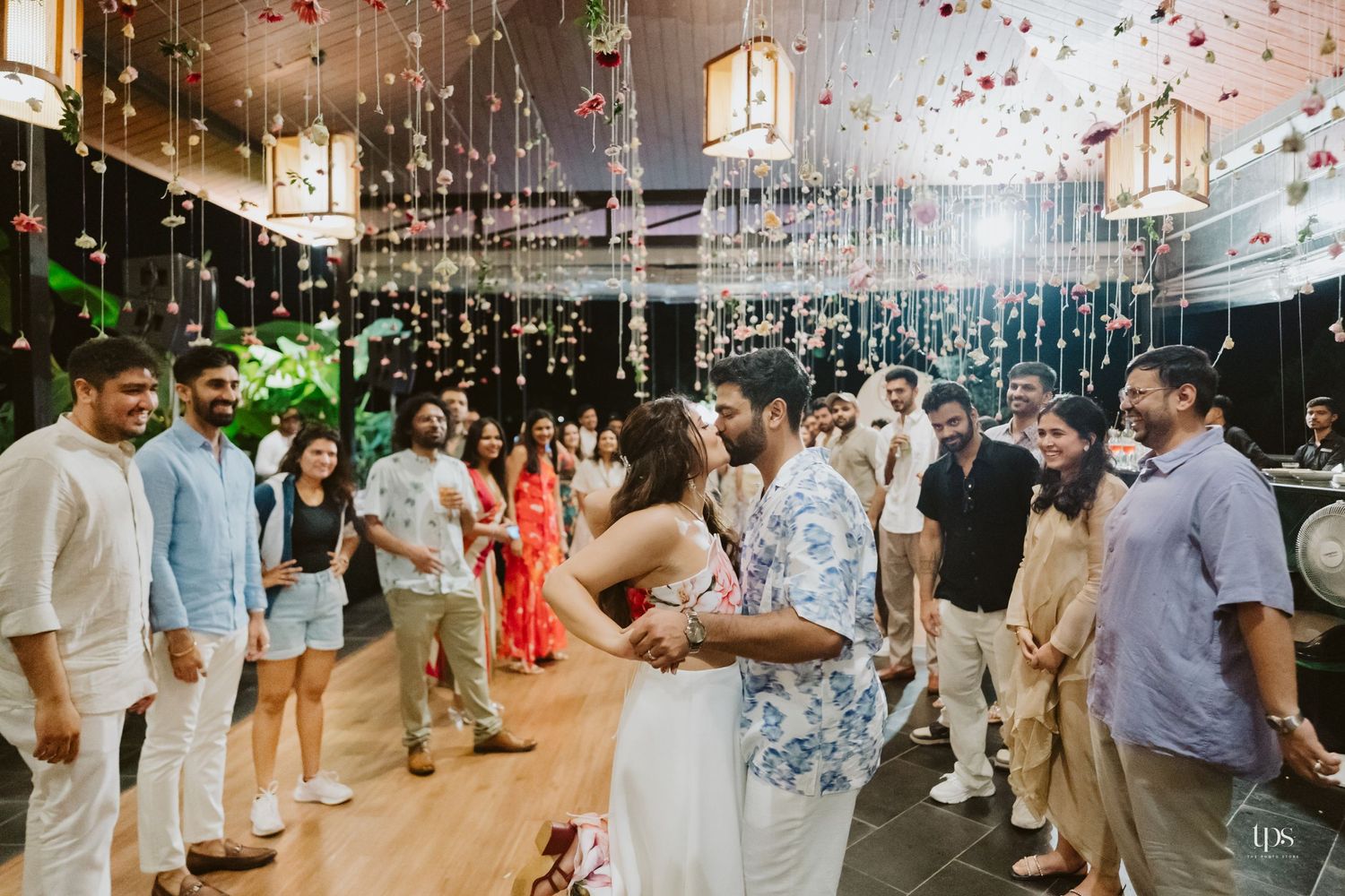 Wedding reception venue decorated with hanging lights and filled with dancing guests.