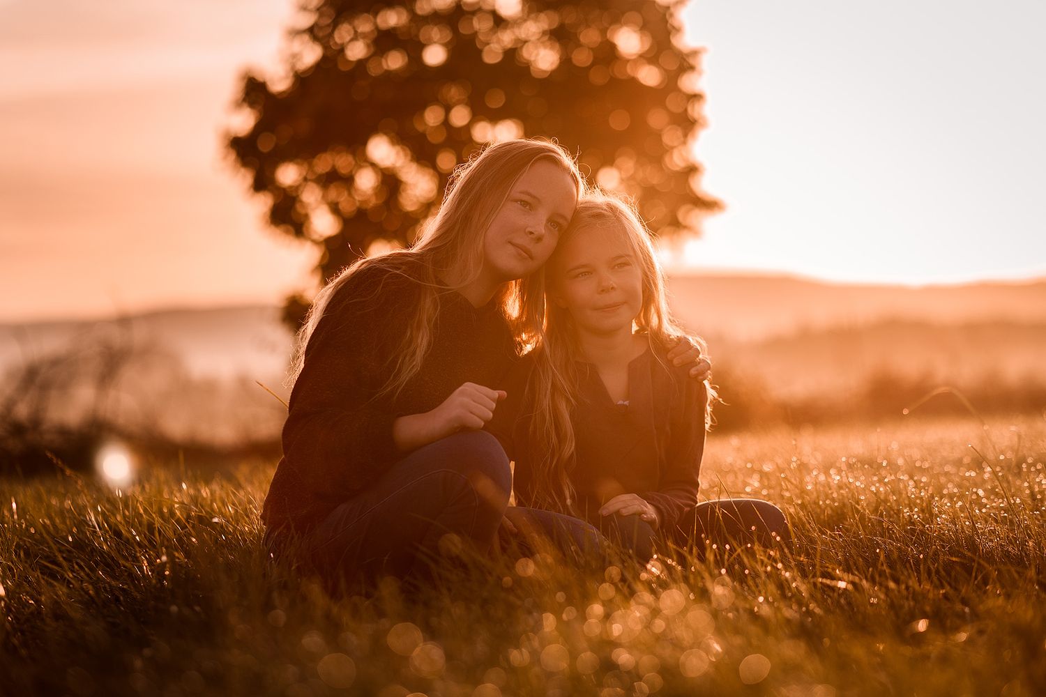 Zwei Kinder sitzen auf Wiese im Sonnenaufgang