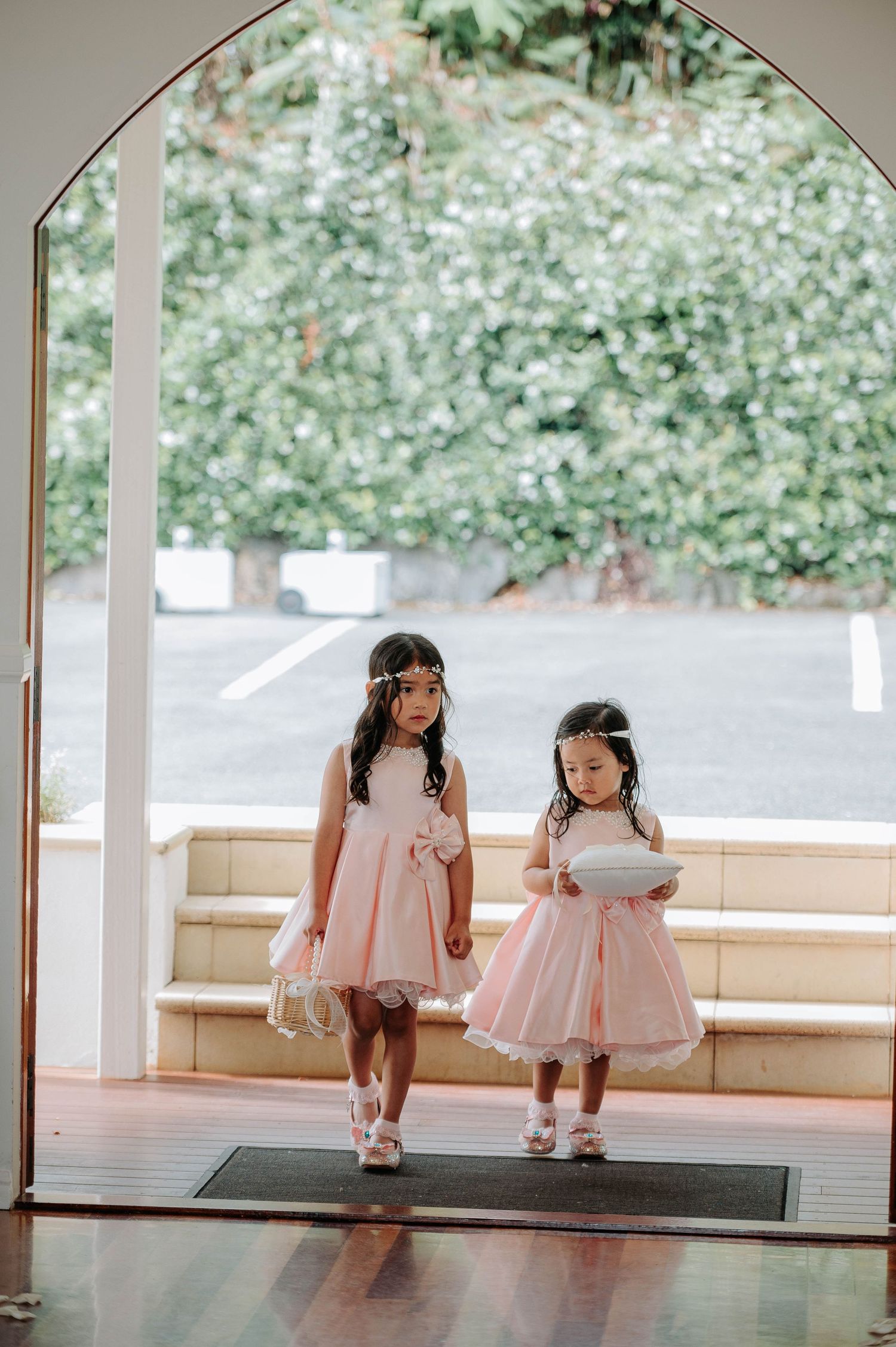 Two flower girls in pink dresses stand under an arched doorway.