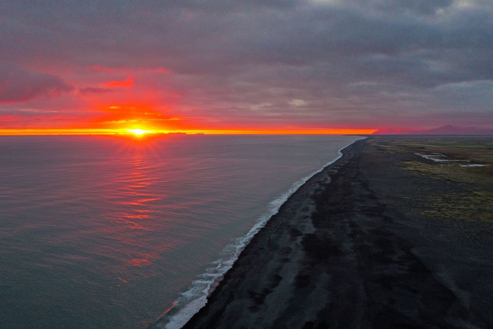 Dramatic sunset over black sand beach coastline in Iceland with fiery orange sky reflecting on ocean waters.