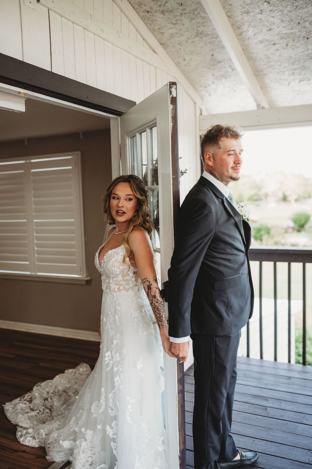 Couple holding hands during first look on porch with dramatic lighting.