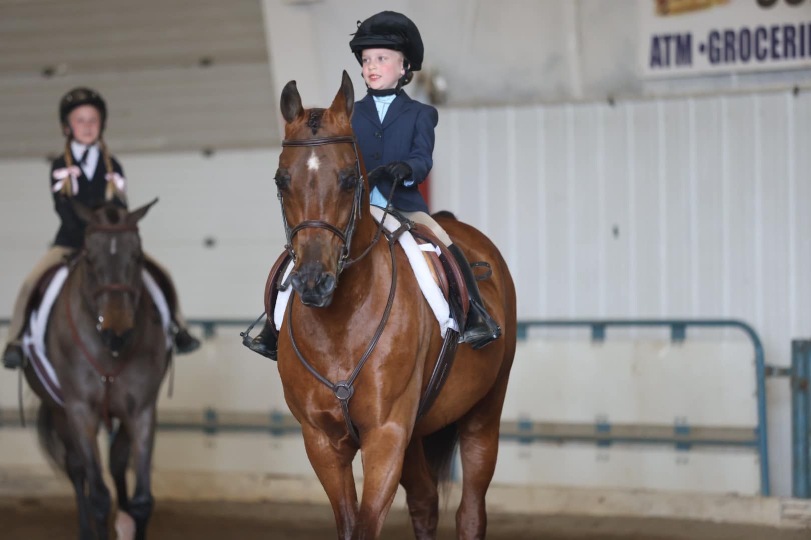 Horses and riders competing in an indoor arena during an equestrian event.