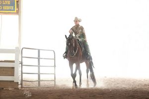 A horse and rider practicing barrel racing in an indoor arena with bright lighting and metal railings.