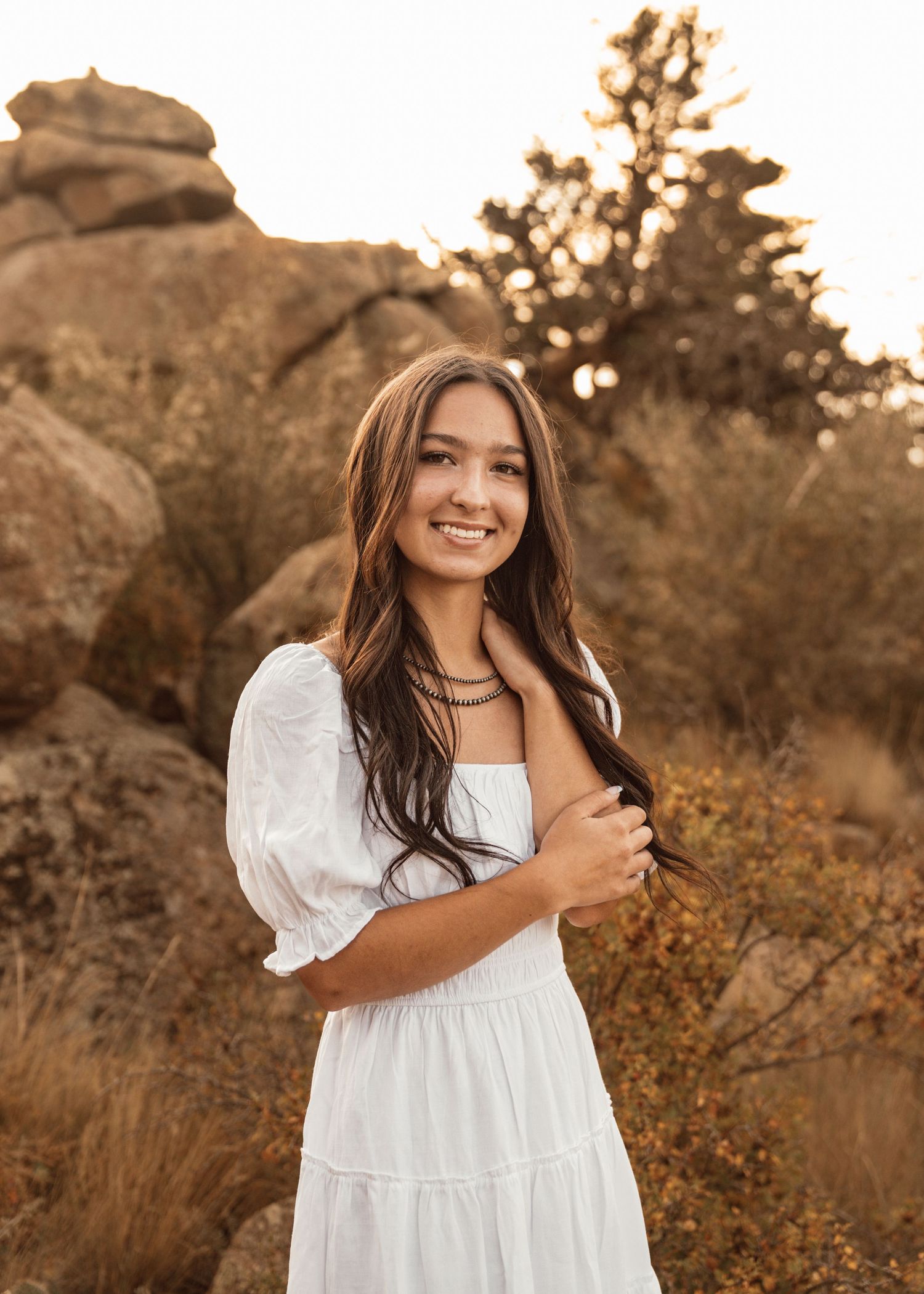 Person in white dress smiles brightly against desert landscape at sunset.