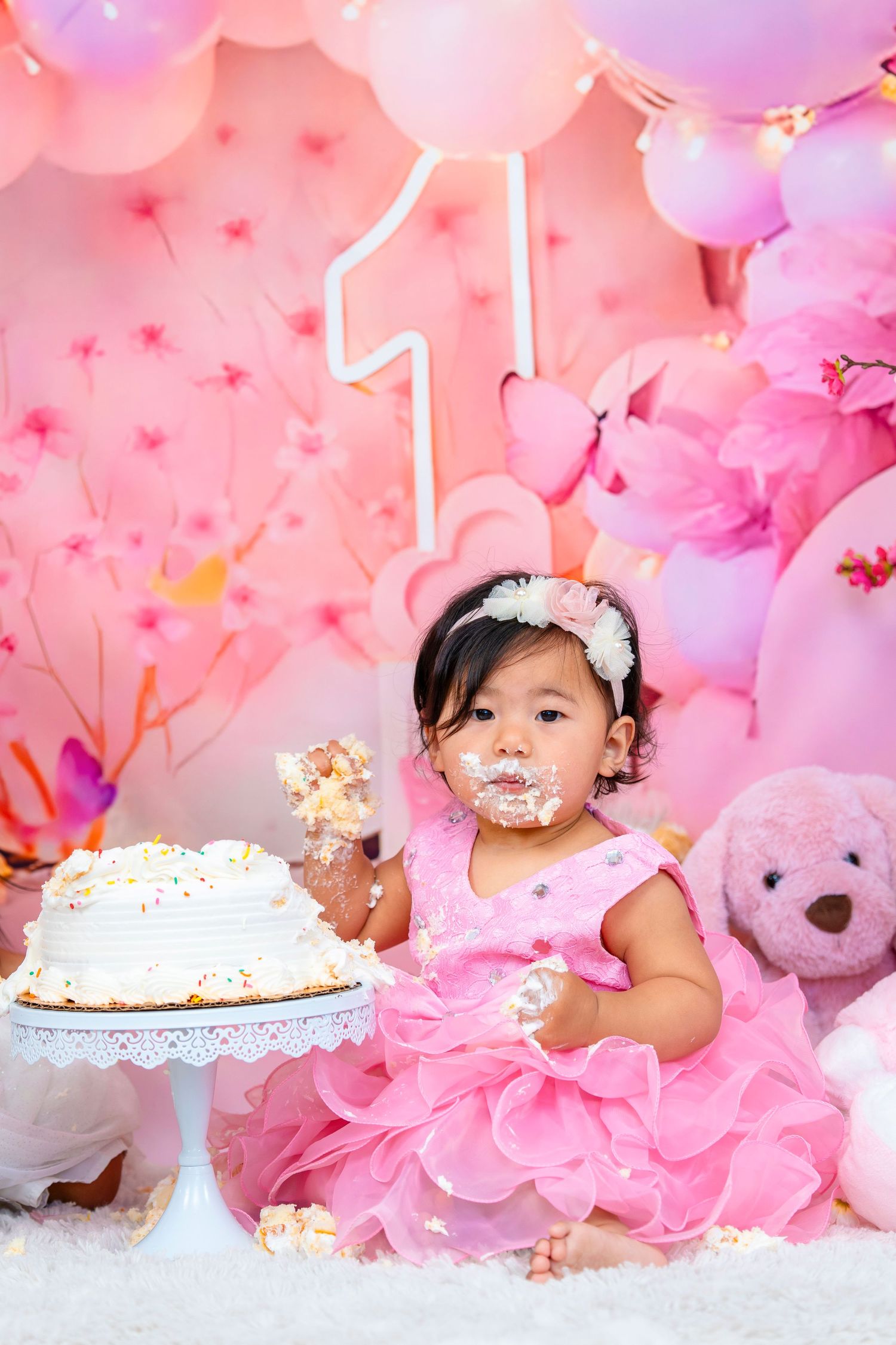 Baby girl with frosting on face during first birthday cake smash photoshoot.