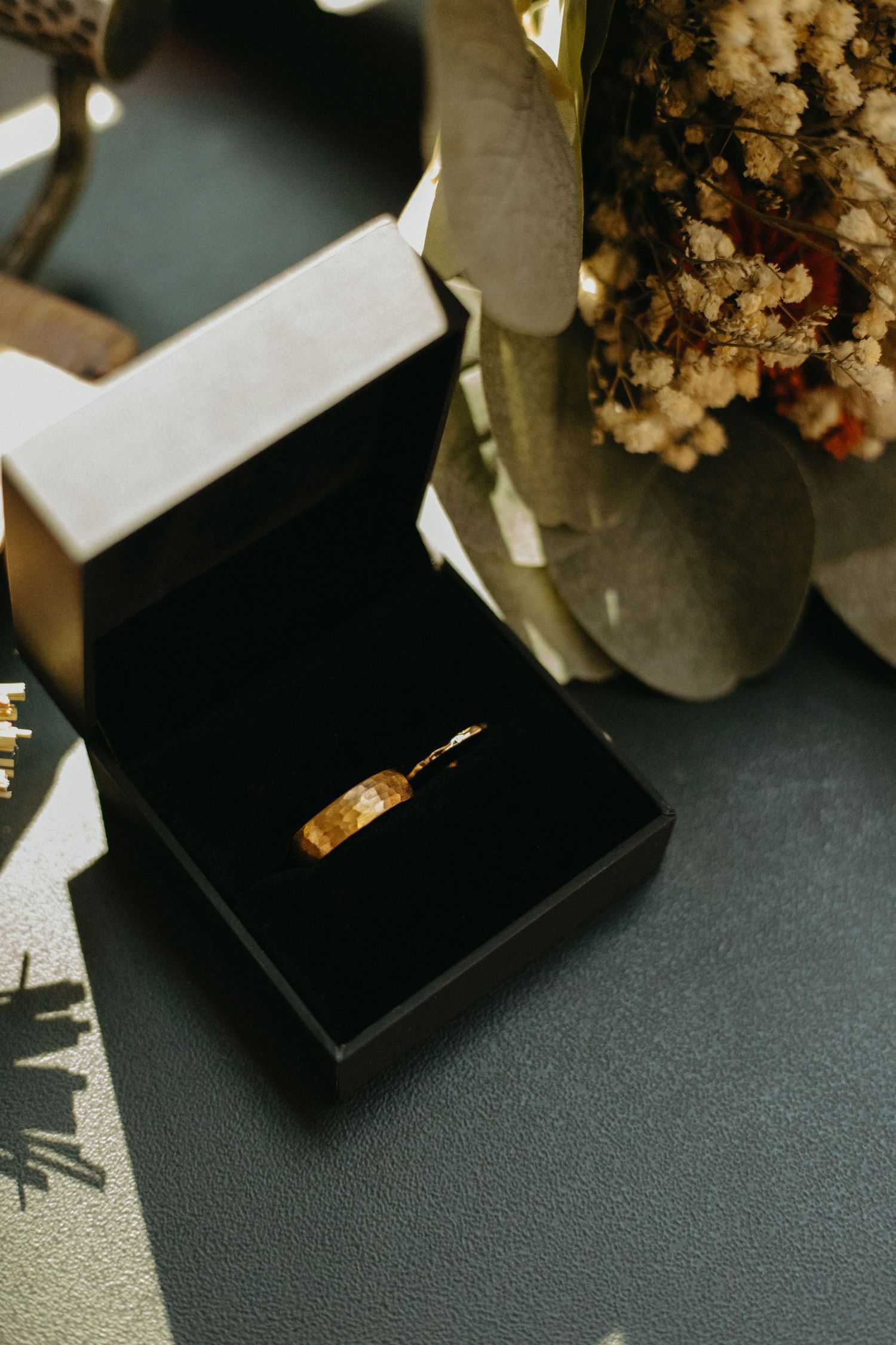 Wedding ring box with dried flowers on a dark textured surface.