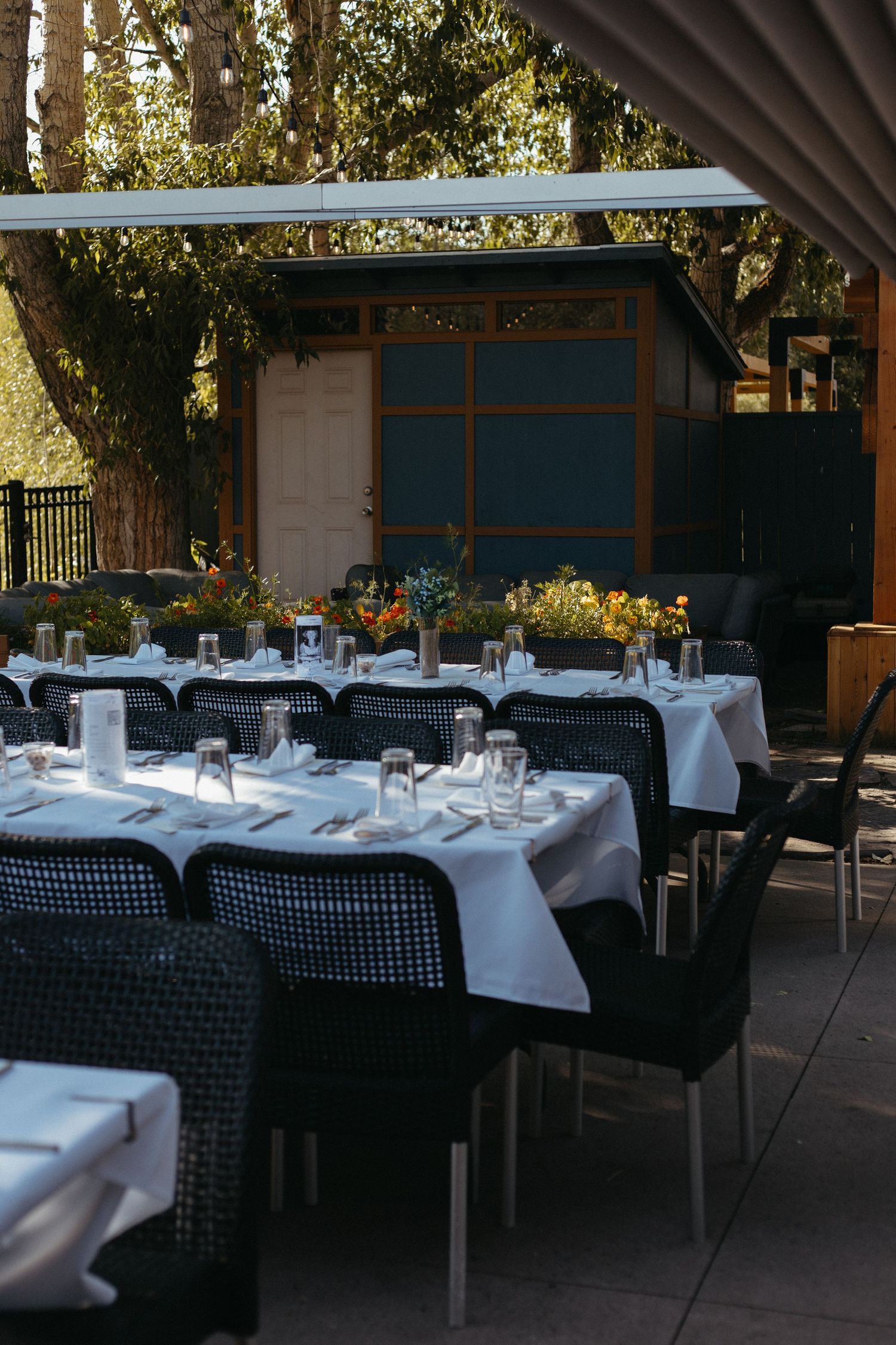 An outdoor wedding reception venue with white tablecloths and black chairs.