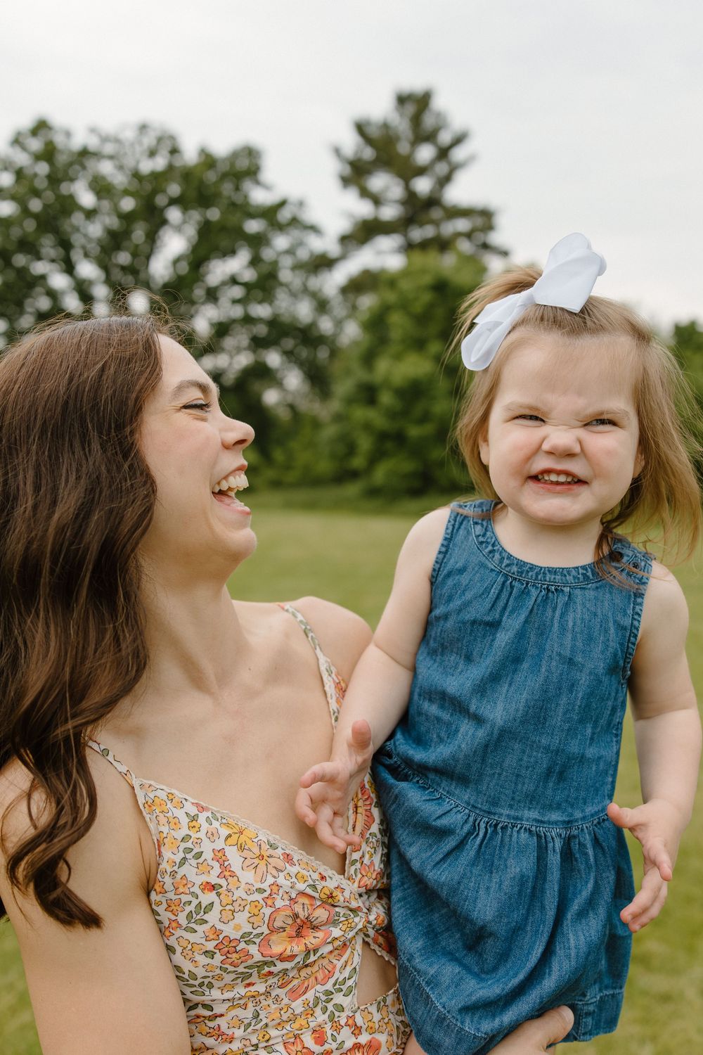 Woman in floral dress and child in blue dress sharing a happy moment outdoors.