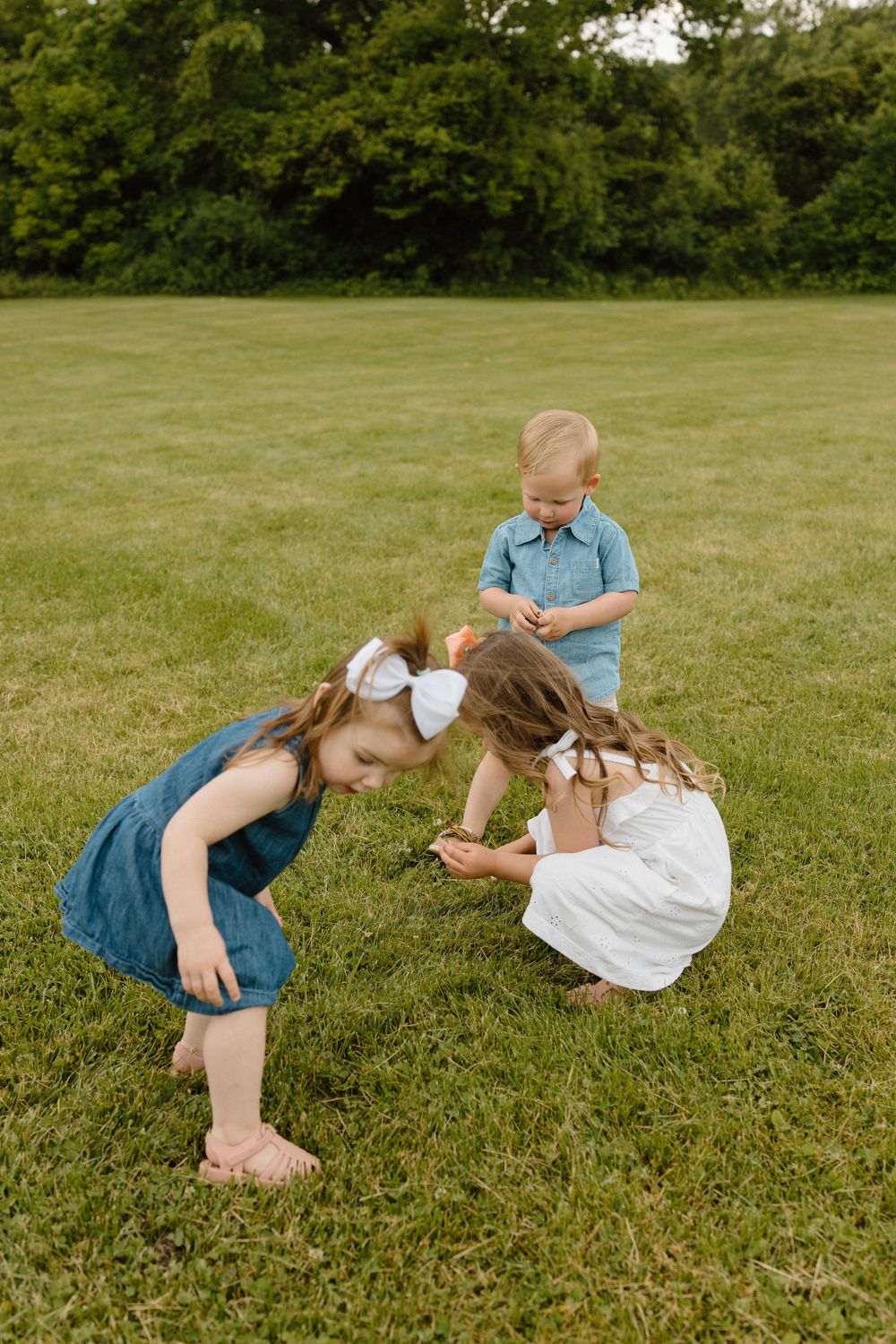 Children playing and bending down together on green grass with trees in background.