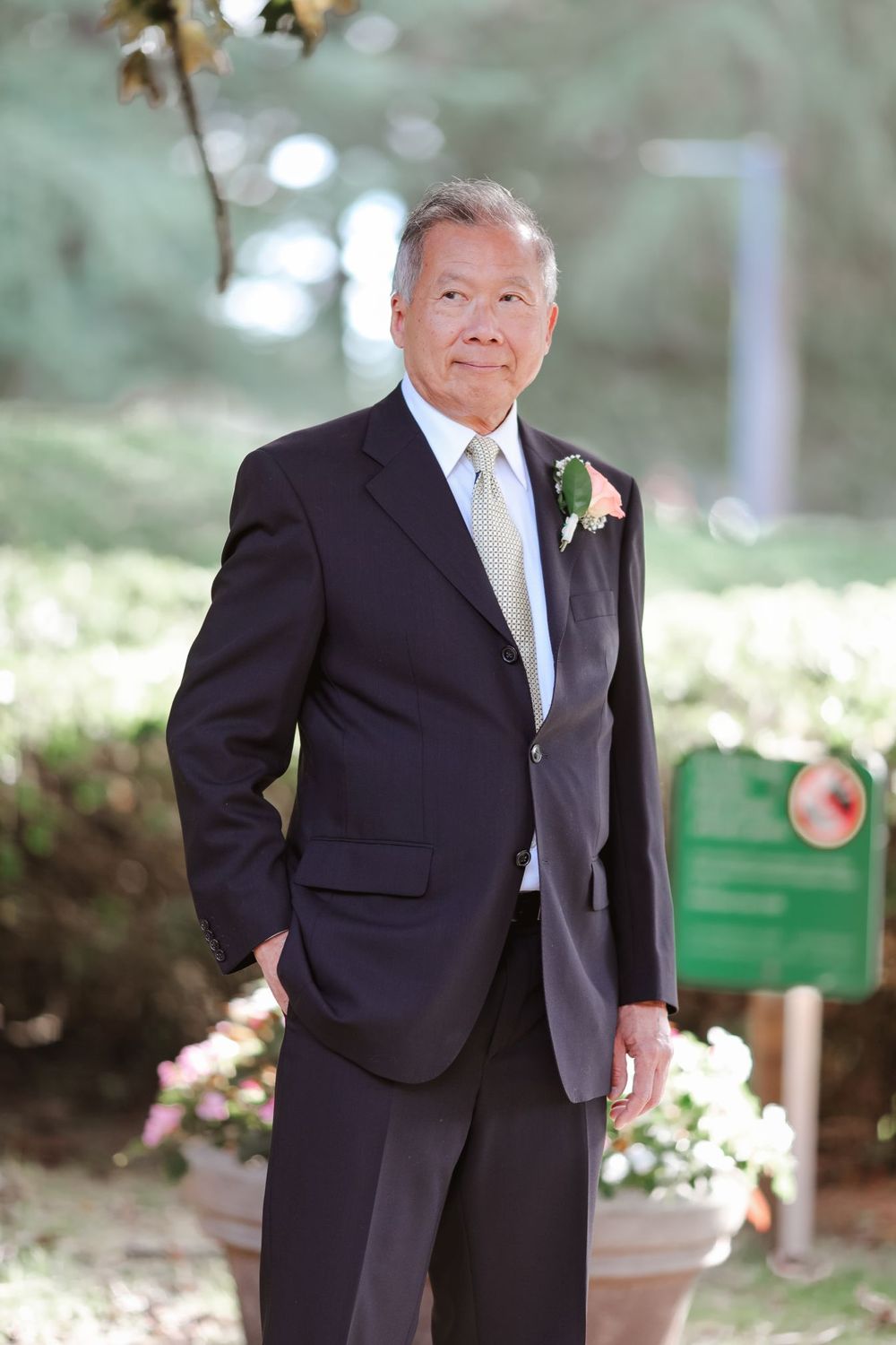 Groom in classic black suit with pink boutonniere in garden setting.