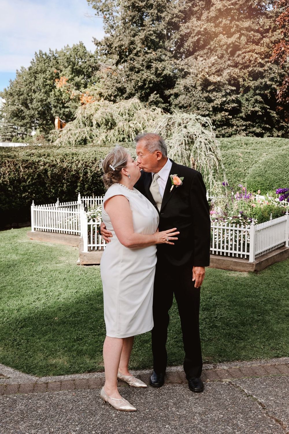 A couple shares a romantic moment in a garden setting with white picket fences.