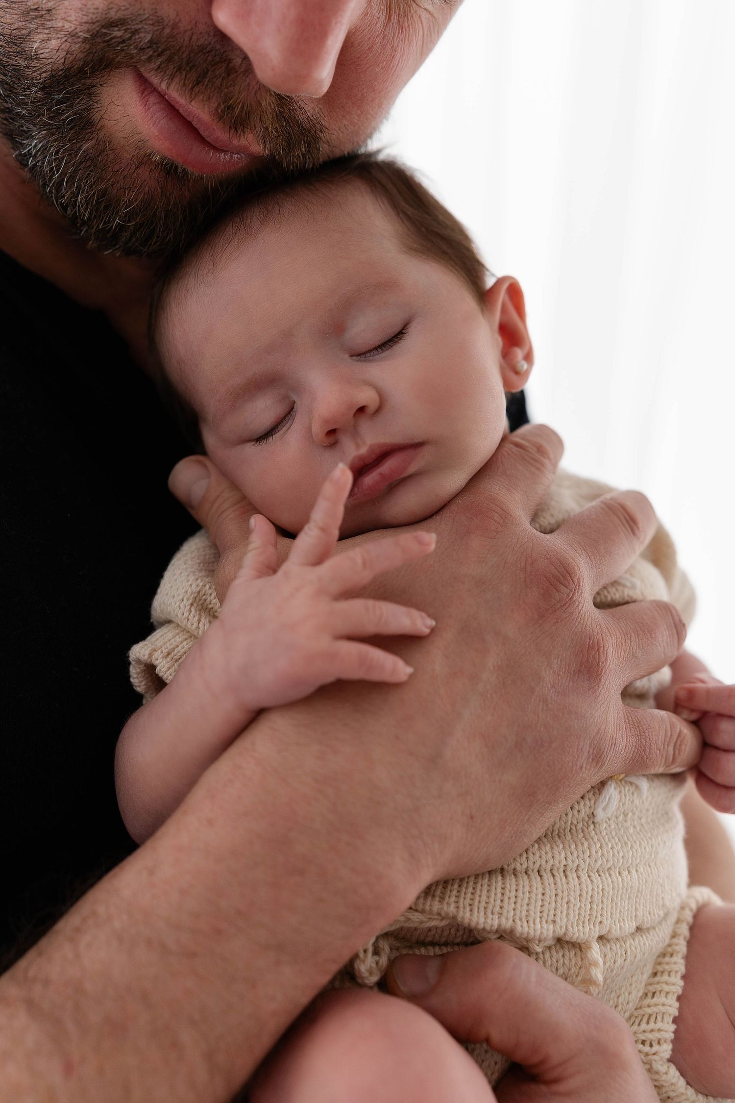 Sleeping infant in cream sweater nestled against adult with beard.