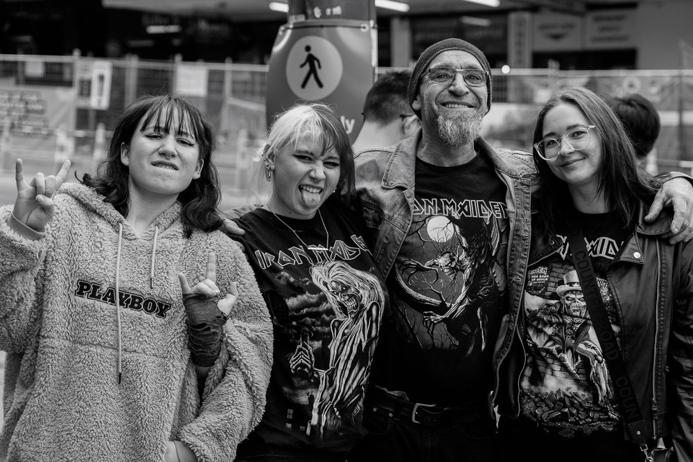 A father and 3 daughters smile while wearing heavy metal t-shirts in a downtown street.