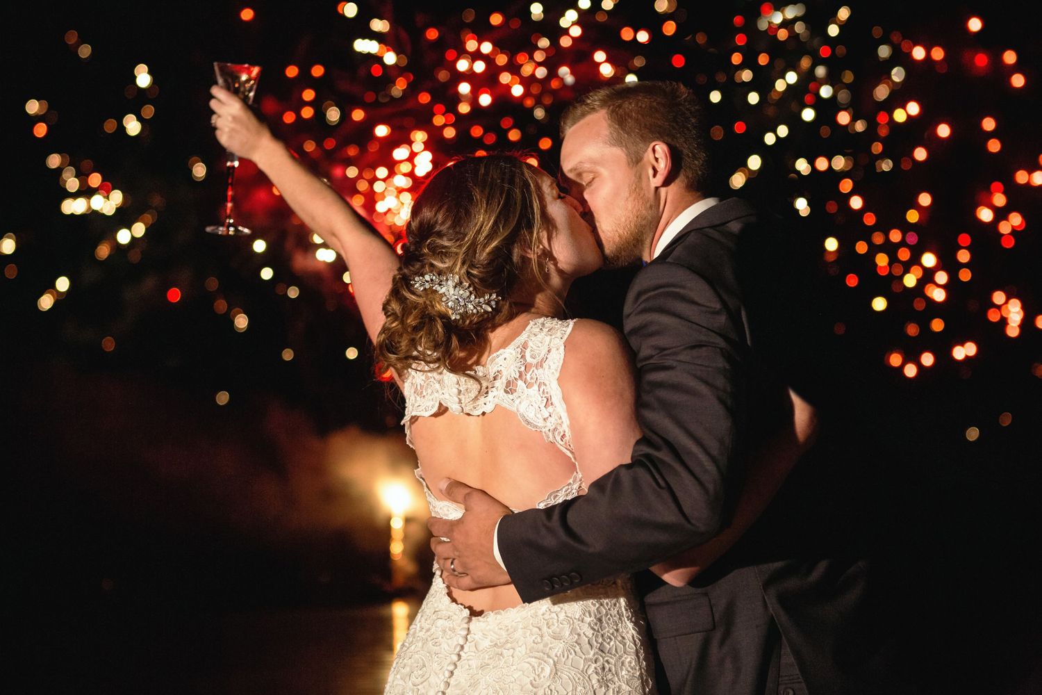 Bride and groom share romantic kiss under sparkling bokeh lights at night.