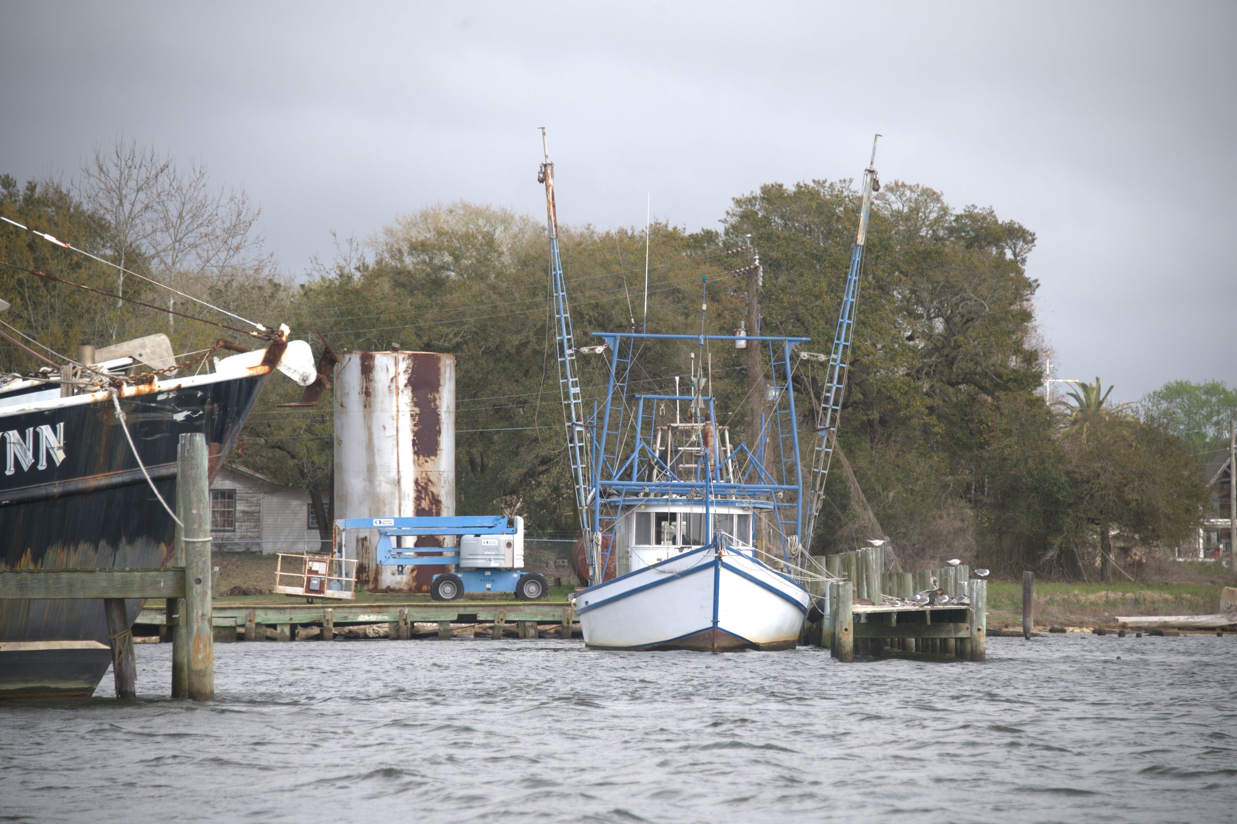 Working waterfront with shrimp boat and rusted fuel tank on Pascagoula Mississippi bayou