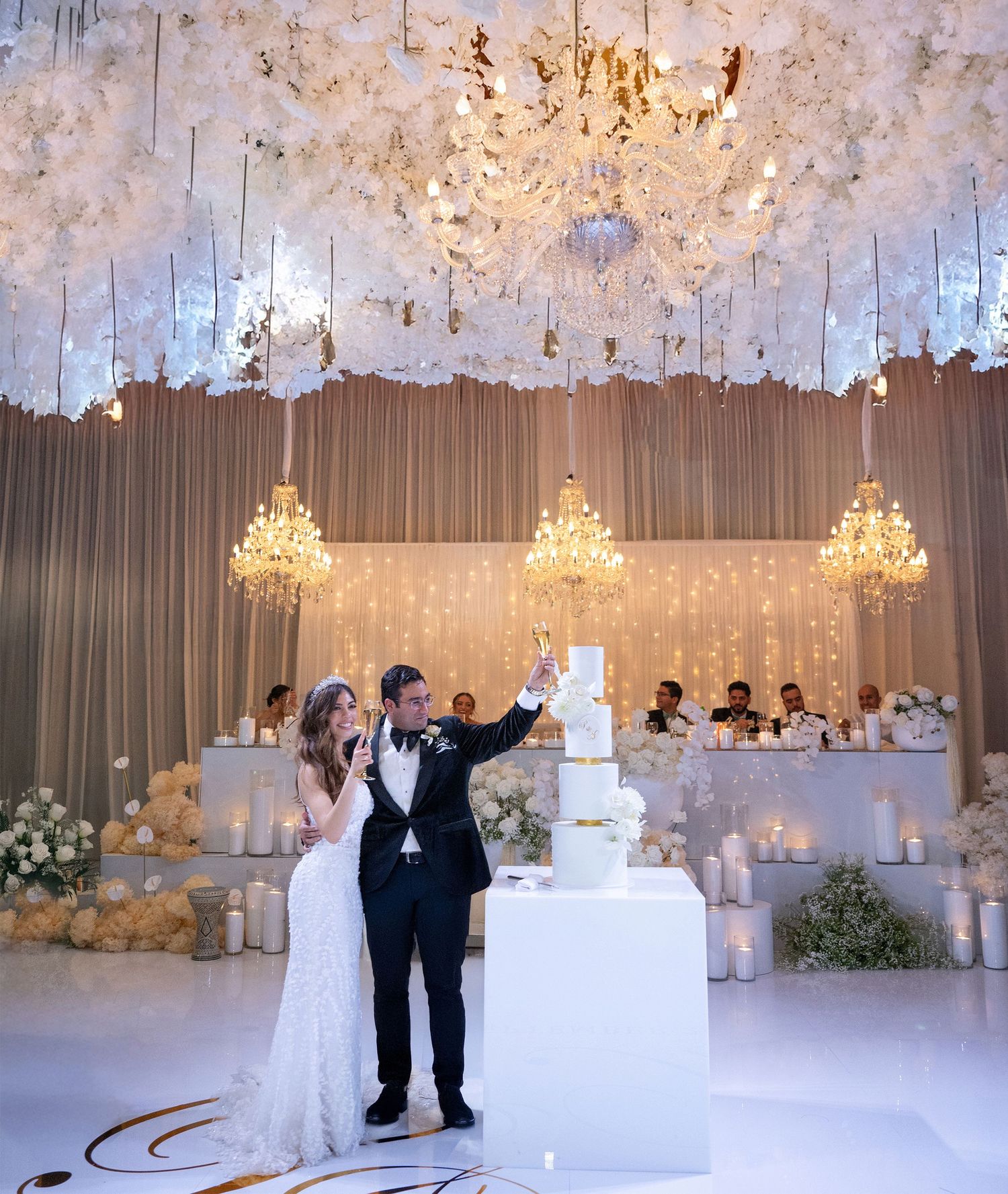 Bride and groom cutting a white wedding cake in a stunning luxury white floral reception venue.