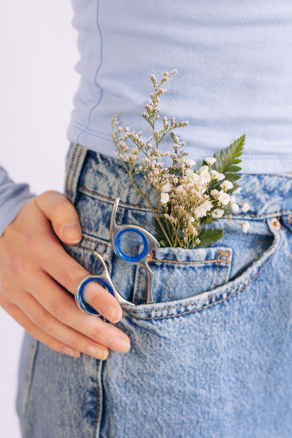 Person in blue jeans holding glasses near pocket with small white wildflowers and green ferns tucked inside.