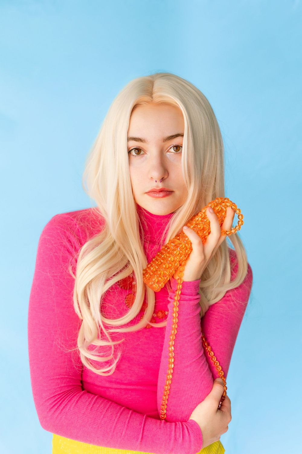Blonde woman in pink turtleneck holding orange knit phone against blue background.