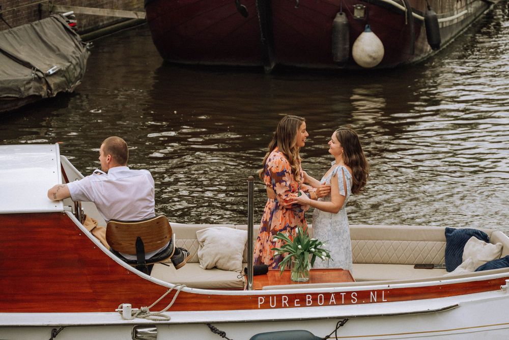 Two women during secret proposal photoshoot on a classic wooden boat  on an Amsterdam canal.