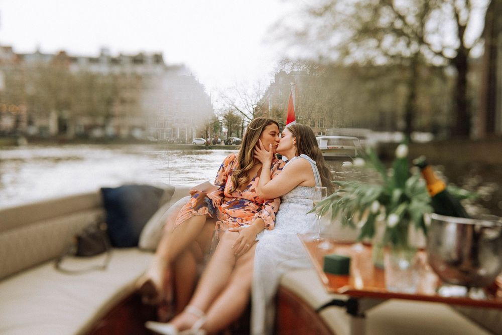 Two women share an intimate moment on a romantic boat ride along an Amsterdam canal.