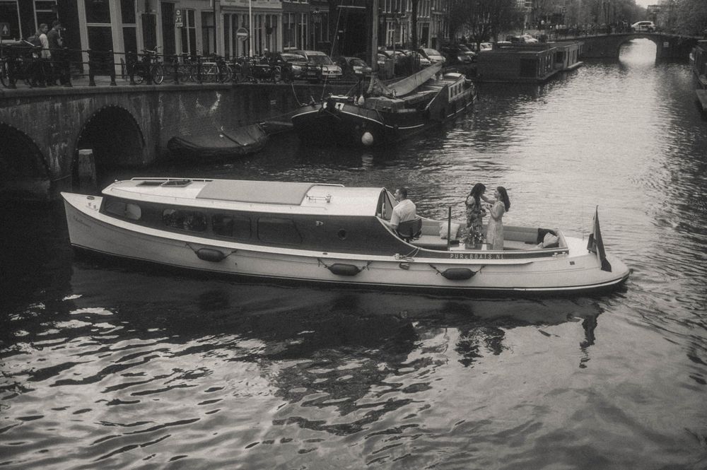 Black and white photo of a classic canal boat cruising through Amsterdam waterways with passengers - Amsterdam Secret proposal.