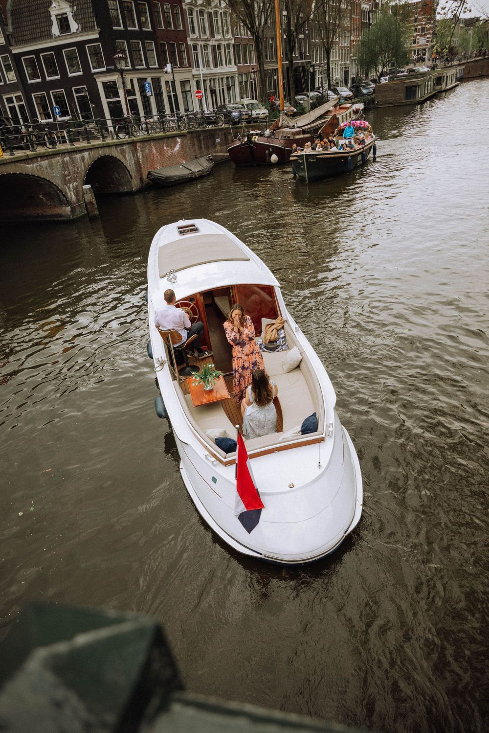 White luxury boat cruising Amsterdam canal with passengers enjoying scenic waterway views near historic bridge.
