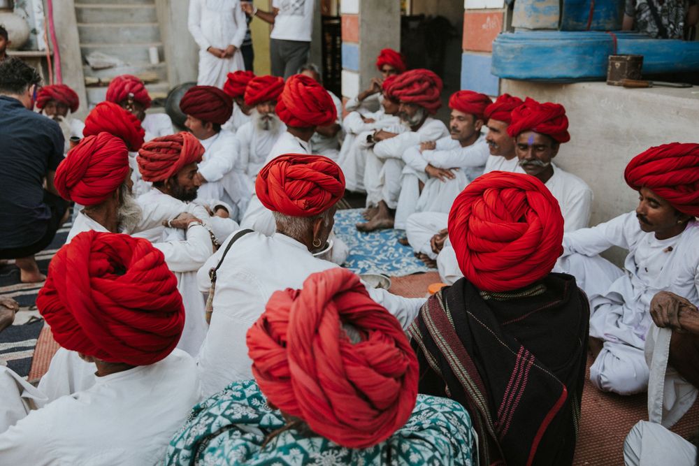 Group of Indian men in traditional white clothing and vibrant red turbans sitting together at a cultural gathering.