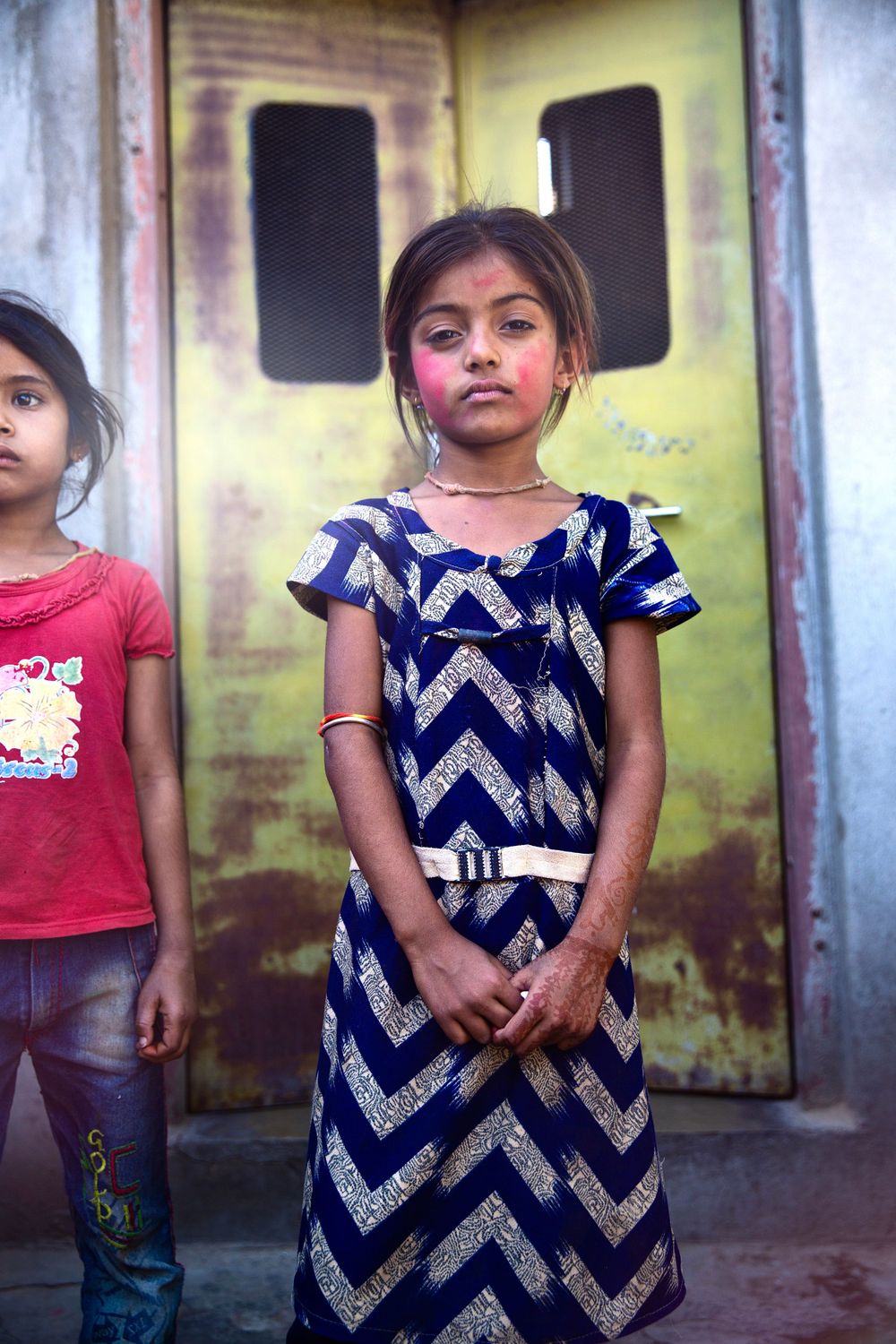 Young Indian girl in blue chevron dress with pink holi powder on her face standing outdoors.