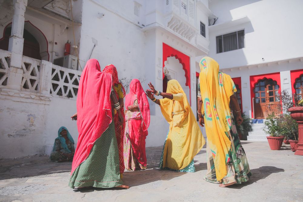 Colorful group of Indian women in bright saris walking through a white courtyard with red architectural accents.