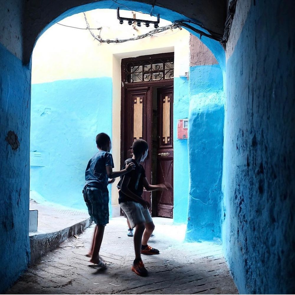 Two children playing in a blue-walled archway leading to a wooden door in a colorful alley.