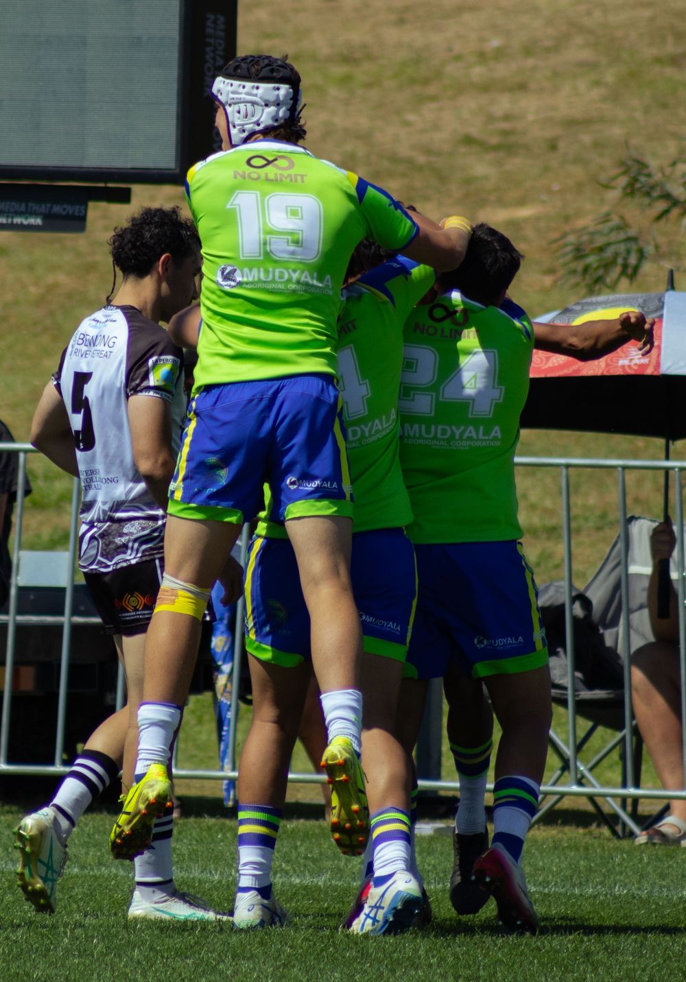 Rugby league players in green and blue Mudyala jerseys celebrating on field during a match.