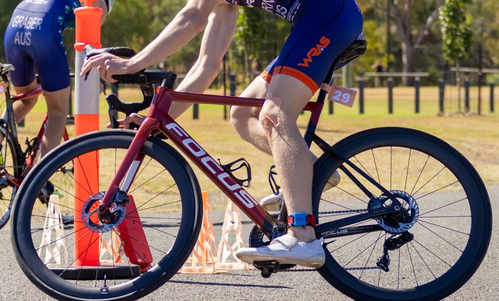 Triathlete riding a red racing bicycle during a triathlon event on a road course.