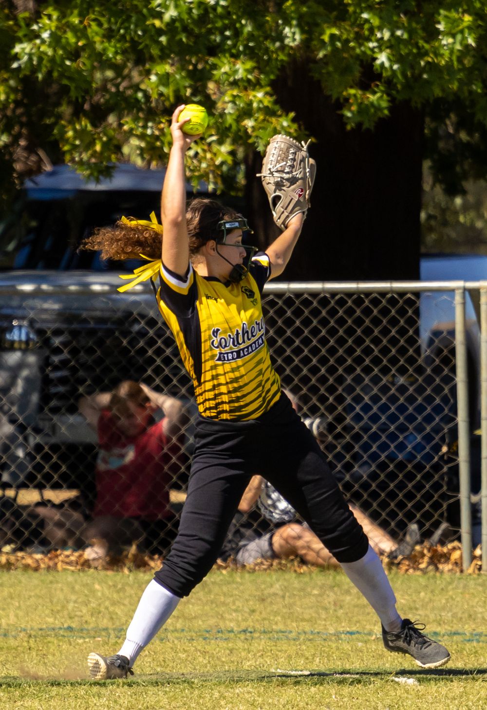 A female softball player in yellow uniform prepares to throw a ball during a game.