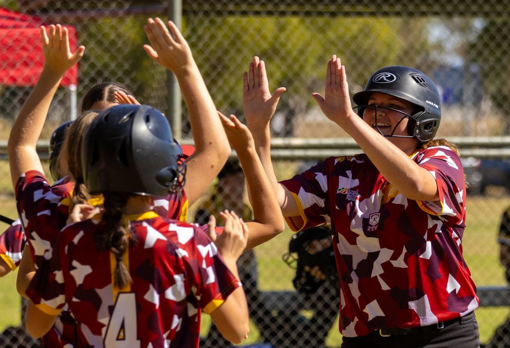 Softball players in maroon uniforms celebrate with high-fives after a successful play during a sunny game.