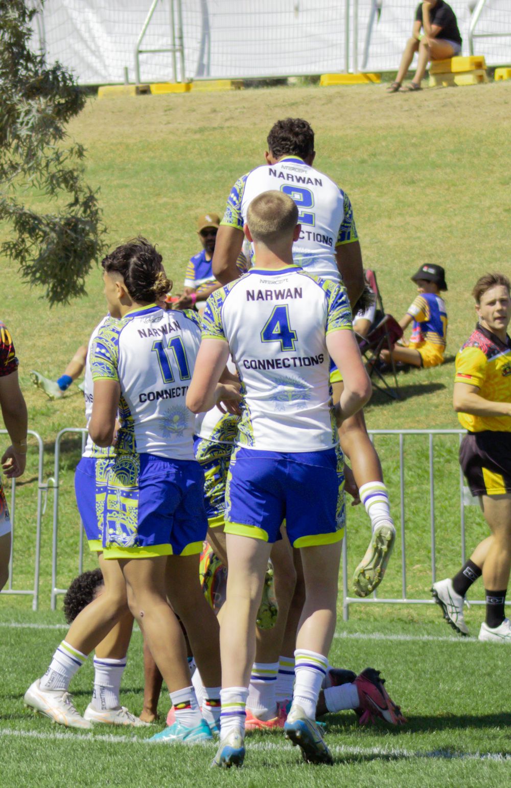 Rugby league players in Narwan Connections uniforms celebrate a try on a green field.