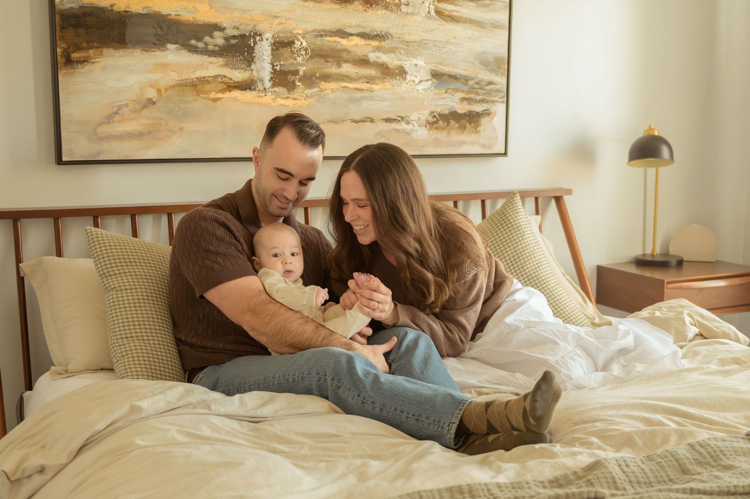 Happy family with parents and baby relaxing together on a cozy bed in a modern bedroom.