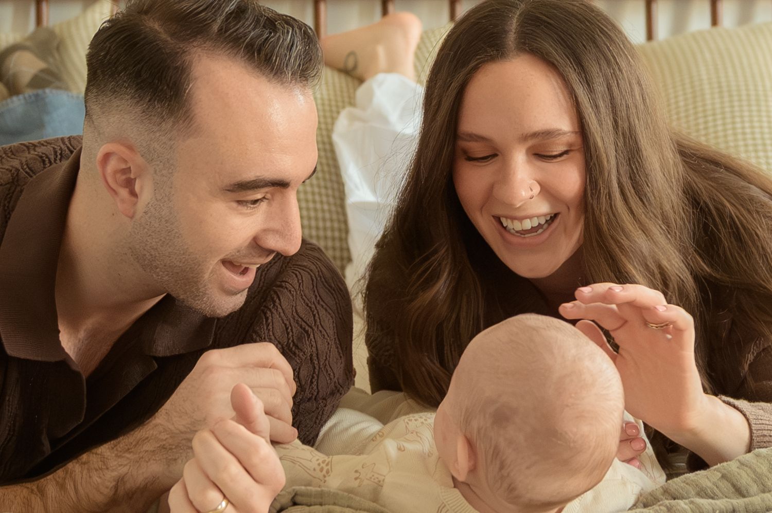Happy couple smiling and bonding with their newborn baby during a warm family portrait session.