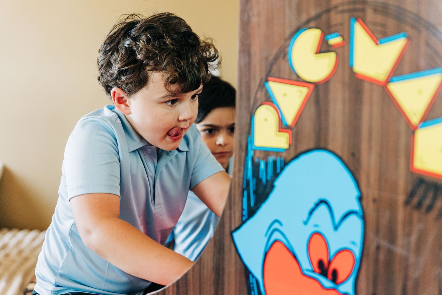 Two young boys playing a Pac-Man arcade game, excitedly leaning in to look at the colorful cabinet.