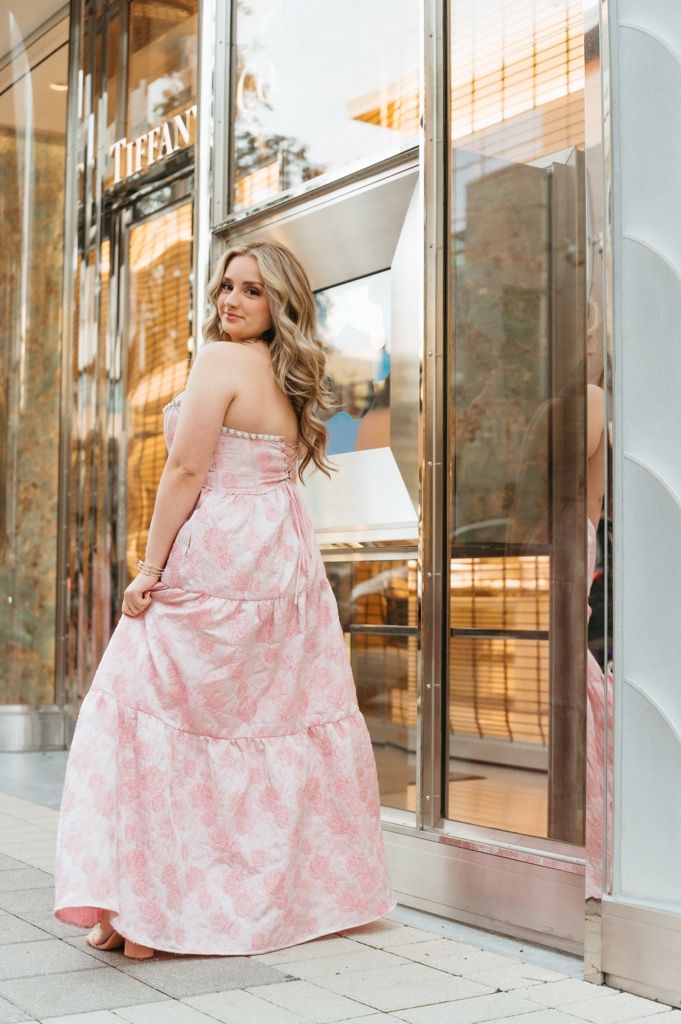 Young woman in pink floral strapless maxi dress posing outside Tiffany store.