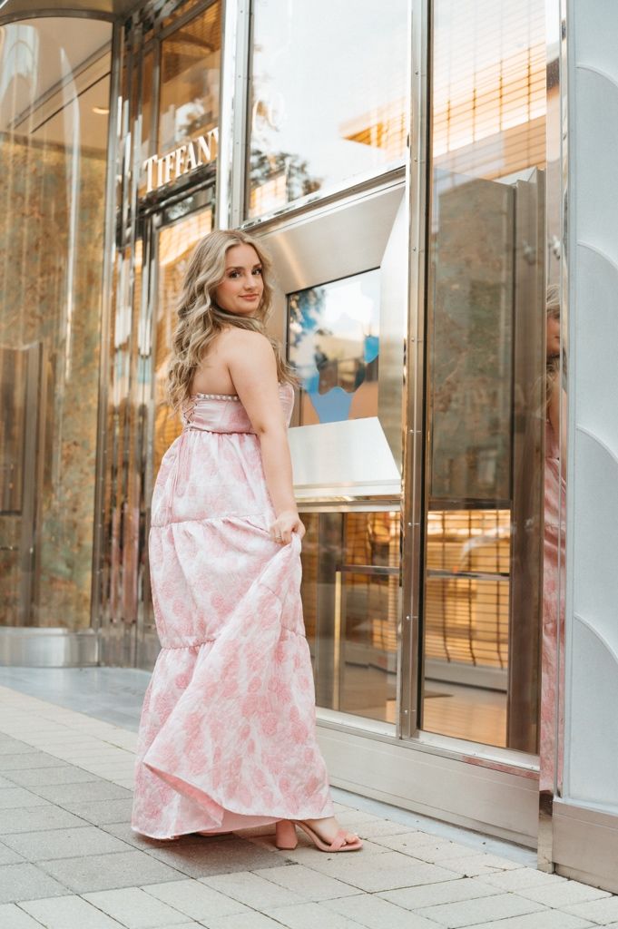 Blonde woman in pink floral maxi dress posing outside Tiffany store.